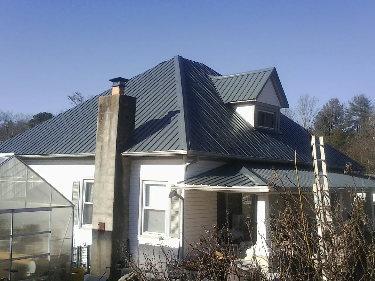 Dark blue standing seam metal roof on a white farmhouse with dormer — Slate & Tile Roof Repair by Roofing Brothers in Anton