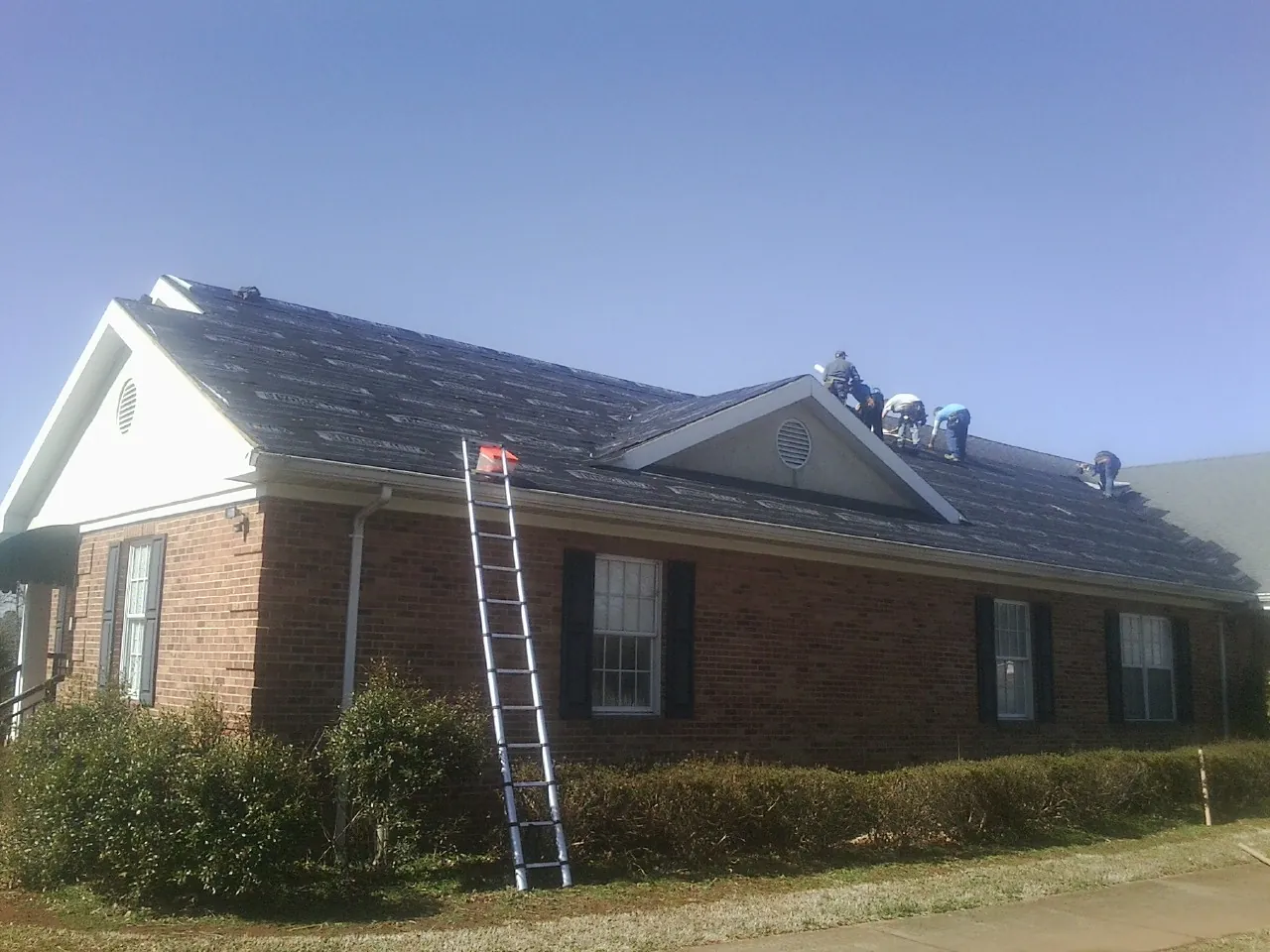 Crew tearing shingles off a brick ranch roof with a ladder set — Metal Roof Repair work by our crew in Anton