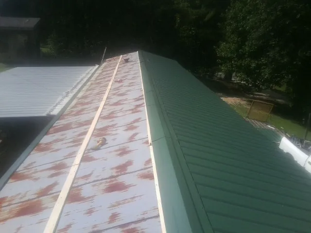 Old rusted panels beside newly installed green metal roofing — Wind Damage Roof Repair by Roofing Brothers in Anton