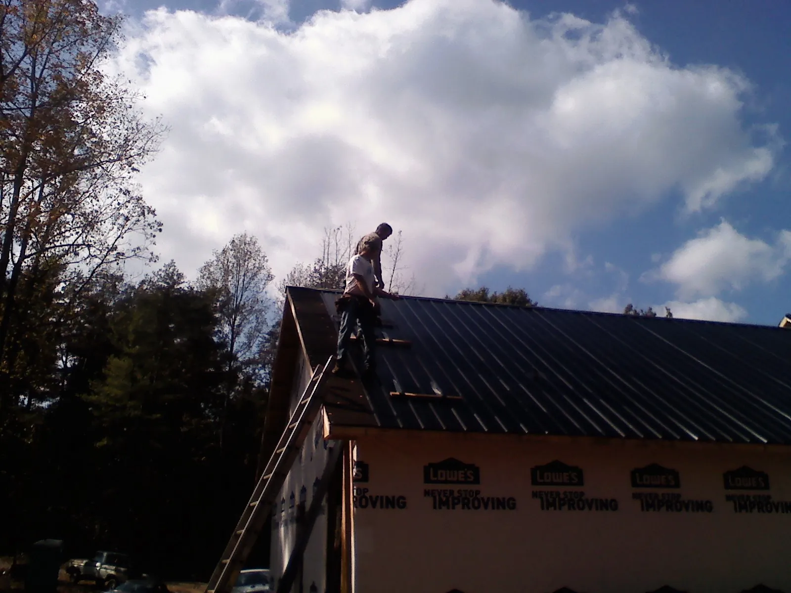 Roofer fastening dark metal panels high against a cloudy sky, from a Roof Inspection job in Anton