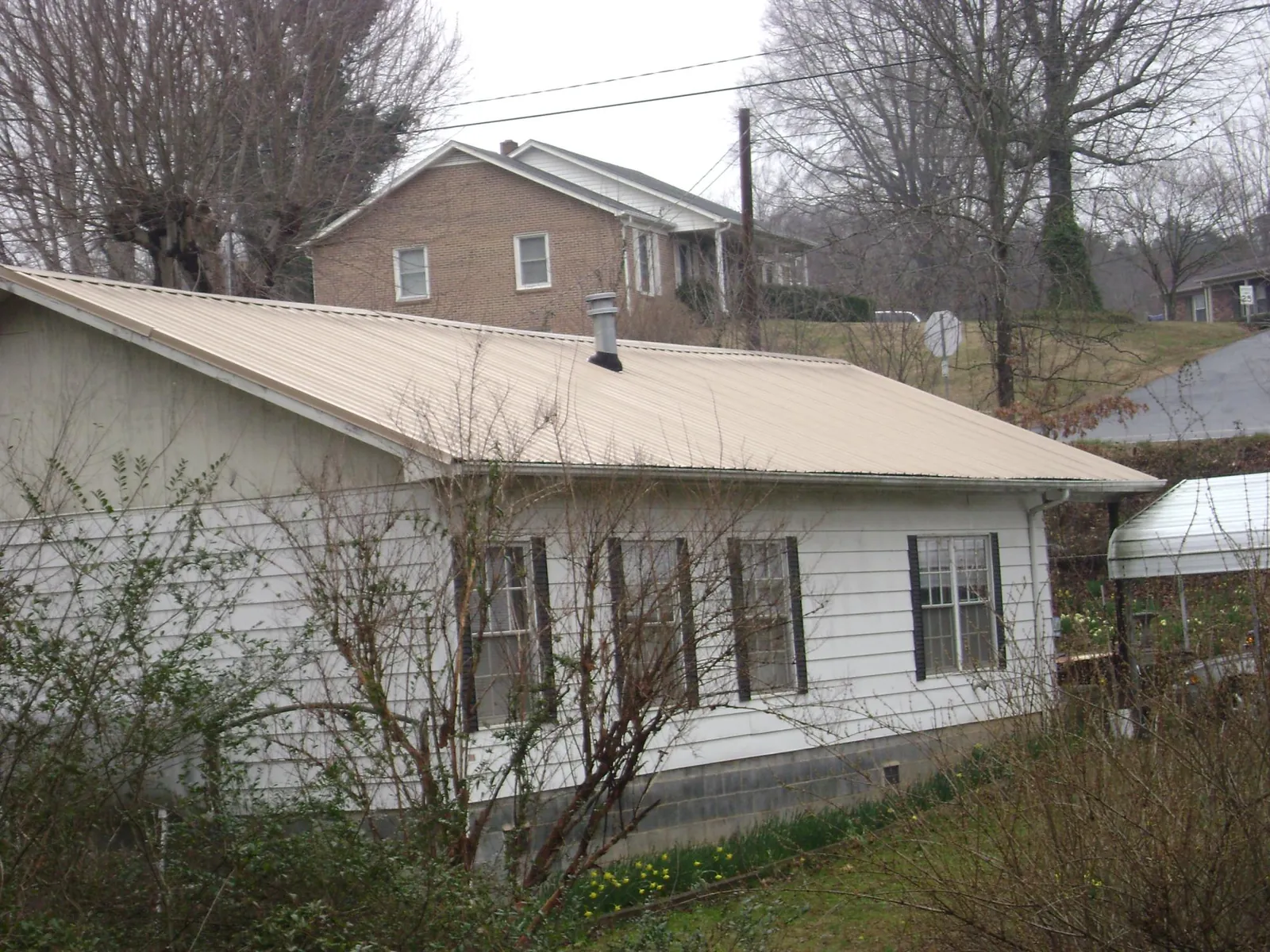 Tan metal roof on a white sided house set into a hillside — Commercial Roofing by Roofing Brothers in Anton