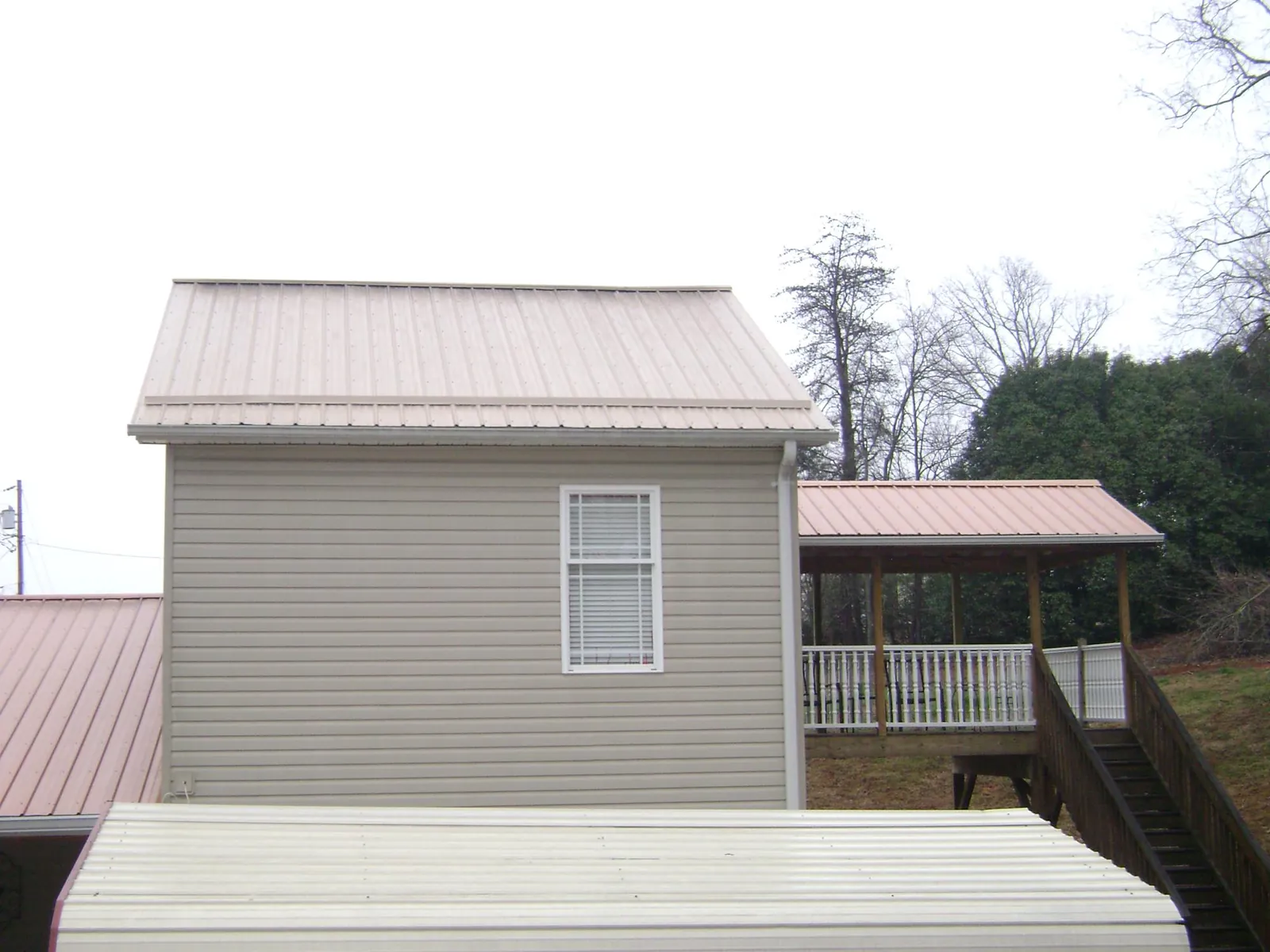 Tan metal roofs on a two story addition and attached porch, from a Roof Replacement job in Anton